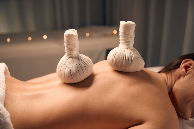 Abgeschnittenes Foto einer Klientin, die während der Behandlung mit Kräuterkugeln auf nacktem Rücken liegt